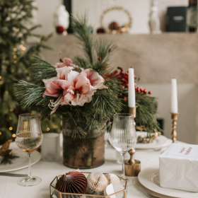 Centre de table de Noël composé de fleurs roses, feuillage hivernal et bougies, idéal pour un dîner festif raffiné et chaleureux. centre-table-noel-fleurs-bougies