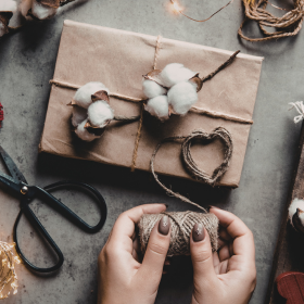 Scène de préparation d’un cadeau fait main avec du papier kraft, de la ficelle et des éléments naturels comme le coton et une décoration en forme de cœur. emballage-cadeau-fait-main-nature