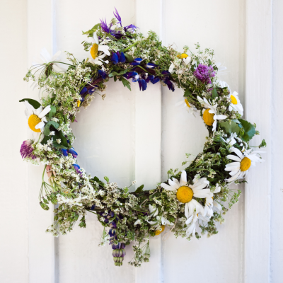 Couronne de fleurs printanières accrochée à une porte, décorée de pâquerettes, de violettes et d’éléments de saison. couronne-printaniere-fleurs-decoration-porte