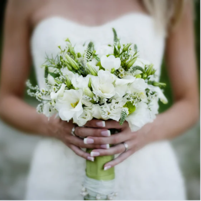 Mariée tenant un bouquet élégant de fleurs blanches aux accents verts, composé notamment de freesias et de feuillages, parfaitement assorti à sa robe blanche pour une cérémonie de mariage raffinée. bouquet-mariee-fleurs-blanches-mariage-elegant