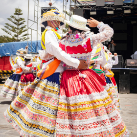 Scène de danse traditionnelle avec des femmes en costumes folkloriques richement colorés. Une ambiance festive et culturelle qui met en valeur les traditions et l’élégance des tenues artisanales. danse-traditionnelle-costumes-folkloriques
