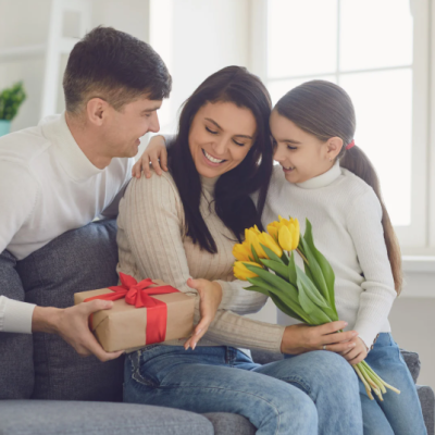 Une mère souriante reçoit un bouquet de tulipes jaunes et un cadeau de la part de son compagnon et de sa fille pour la fête des mères. fete-des-meres-cadeau-tulipes-famille