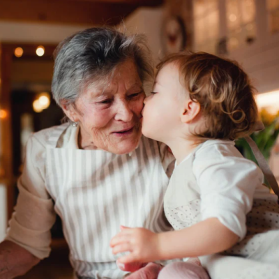 Tendresse entre générations : une petite fille embrasse sa grand-mère dans une cuisine chaleureuse à l’occasion de la fête des grands-mères. fete-des-grands-meres-enfant-embrasse-grand-mere