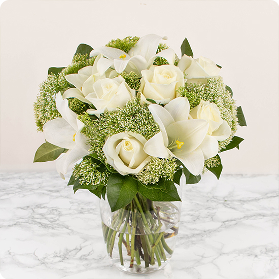 Élégant bouquet pour deuil, composé de belles roses blanches, de petites fleurs de saison et de feuillages fins et délicats.