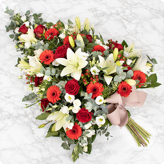 Cette gerbe de fleurs est composée de belles roses, de majestueux lys et d'élégantes fleurs de saison dans les tons rouges et blancs, agrémentées d'un joli feuillage vert tendre.